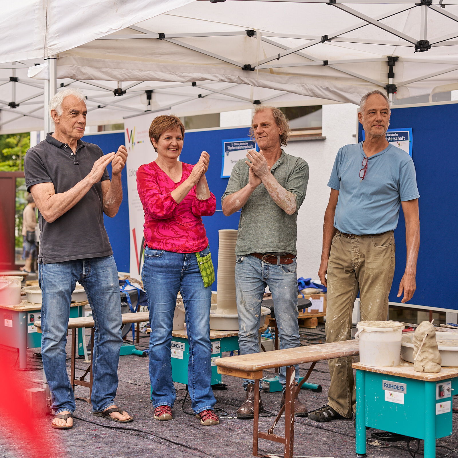 Vier Keramikerinnen und Keramiker applaudieren unter einem Pavillon beim Europäischen Keramikmarkt in Höhr-Grenzhausen © Janos Wlachopulos.