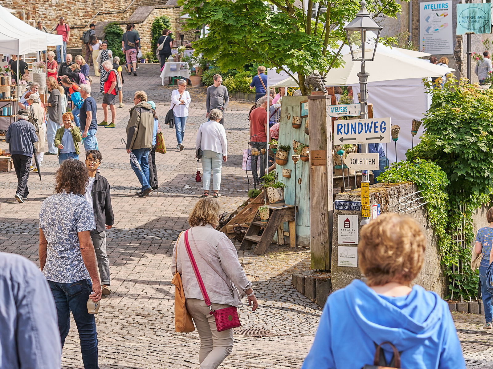 Besucherinnen und Besucher flanieren &uuml;ber den Europ&auml;ischen Keramikmarkt in der Altstadt von H&ouml;hr-Grenzhausen, UNESCO Creative City of Crafts and Folk Art, umgeben von Keramikst&auml;nden, historischem Mauerwerk und sommerlicher Atmosph&auml;re.