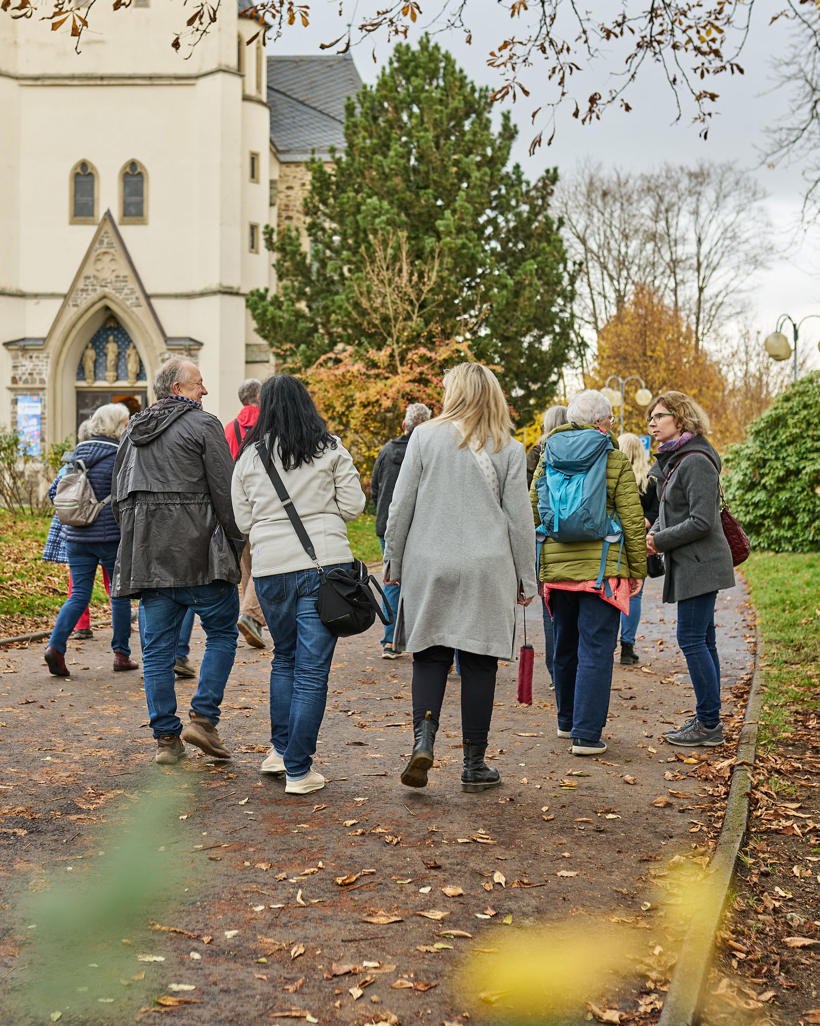 Teilnehmende gehen gemeinsam über einen Weg nahe einer Kirche in Höhr-Grenzhausen beim Stadtspaziergang des Modellvorhabens Innenstadt-Impulse.