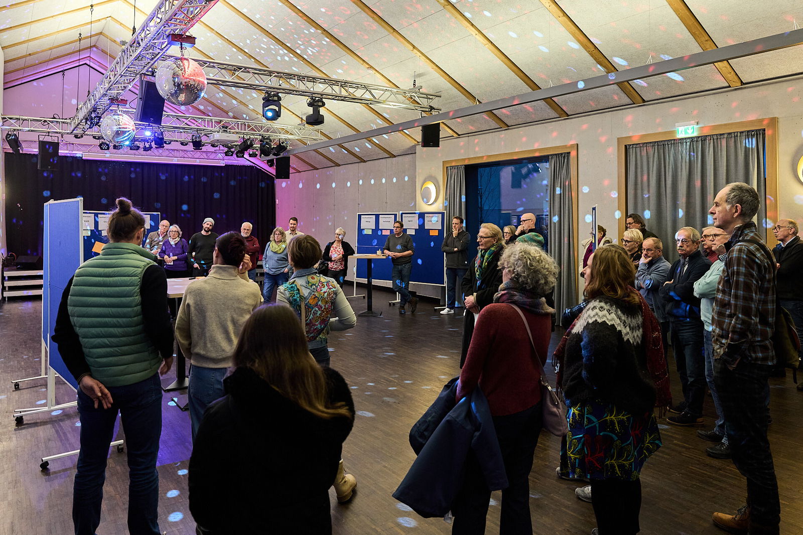 Teilnehmende stehen im Plenum einer Zukunftswerkstatt und diskutieren gemeinsam Ideen zur Innenstadtentwicklung im Rahmen des Modellvorhabens Innenstadt-Impulse und des Projekts Stadt.Idee.Wirkung in Höhr-Grenzhausen.