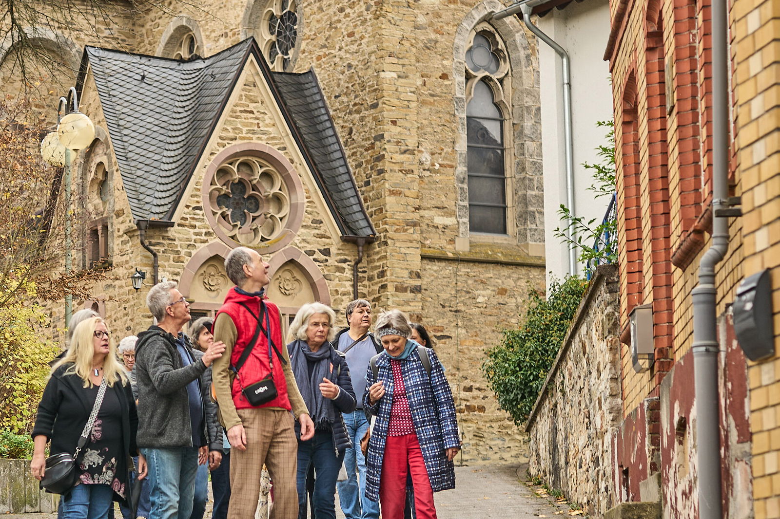 Teilnehmende eines Stadtspaziergangs betrachten gemeinsam die Umgebung nahe einer Kirche in Höhr-Grenzhausen im Rahmen von Stadt.Idee.Wirkung.